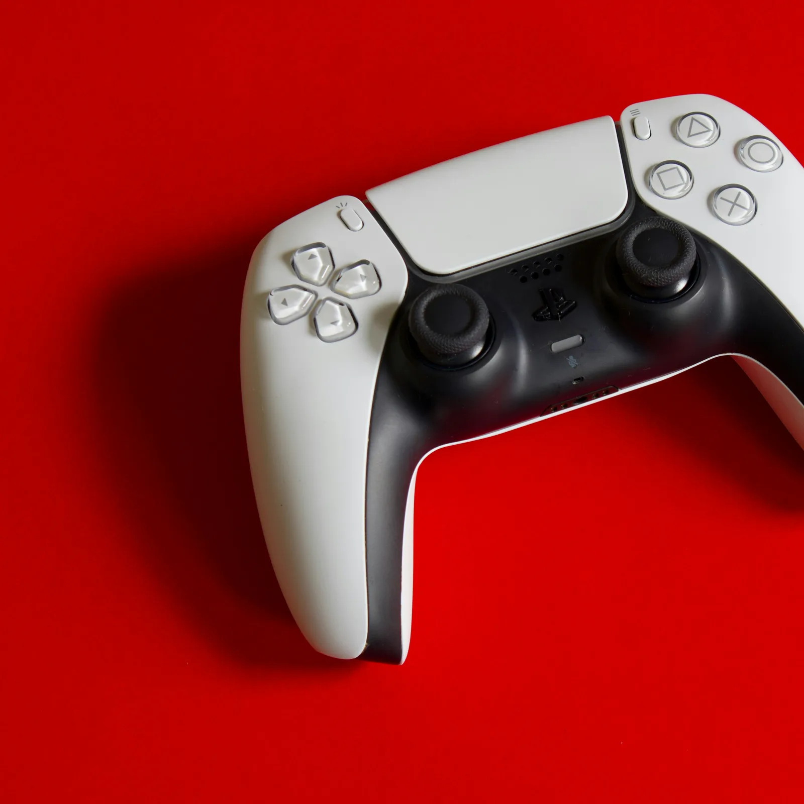 White and black Sony PlayStation 5 DualSense controller on a vivid red surface